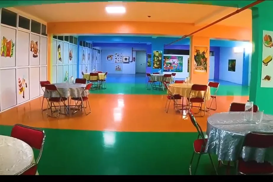 Salle polyvalente de l'établissement, aux murs peints et tables rondes